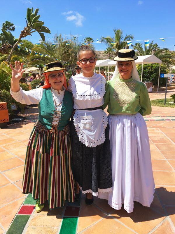 Eine deutsche Praktikantin mit zwei Kolleginnen in kanarischer Tracht – Tradition trifft Austausch unter blauem Himmel. Eine deutsche Praktikantin mit zwei Kolleginnen in kanarischer Tracht vor blauem Himmel als Zeichen für kulturellen Austausch und gelebte Tradition.