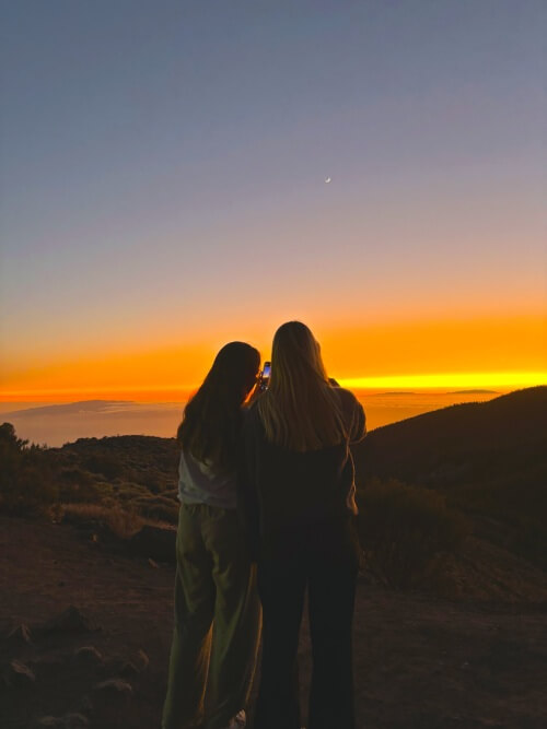 Group of friends watching the sunset from Mount Teide, with vibrant skies and mountain silhouettes.